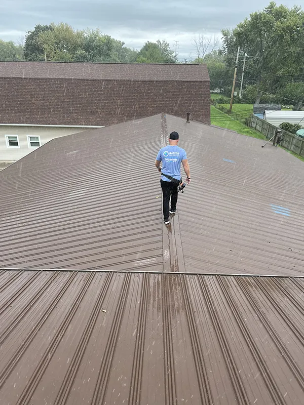 Raptor Roofing is ready for emergencies, demonstrated by our dedicated roofer inspecting a metal roof during a rainy day to ensure quick and reliable service in any weather.