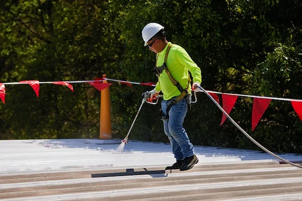 Commercial roofer spraying protective coating across a flat roof surface