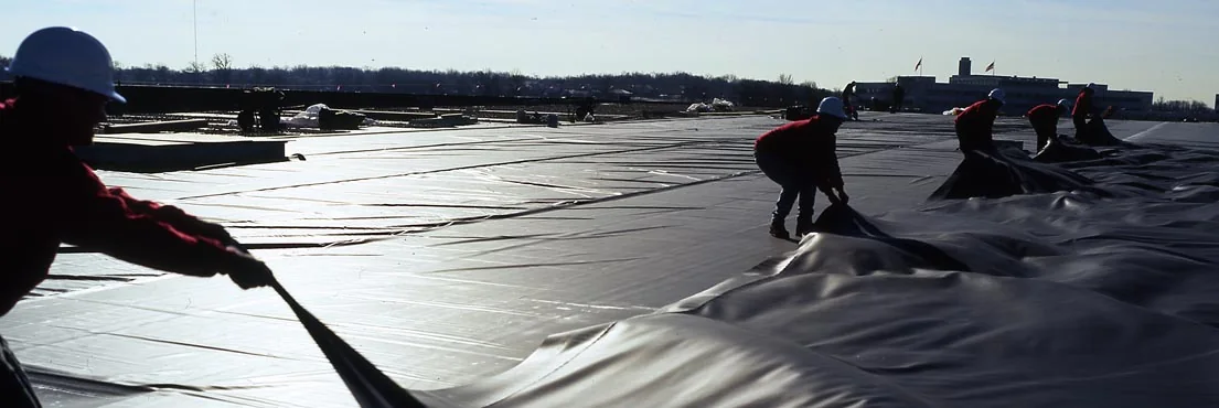 Commercial roof crew installing EPDM rubber membrane on a low slope roof