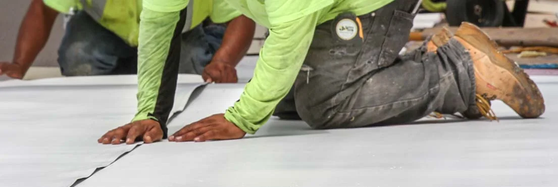 Commercial roofer working along a white TPO roof seam on a low slope building