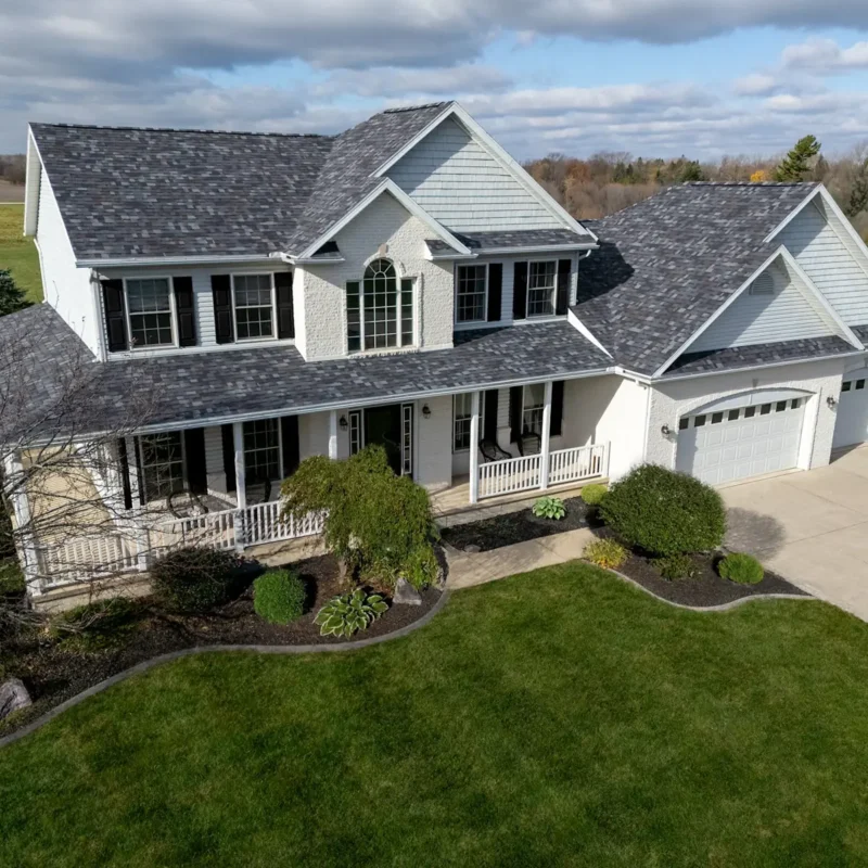 White farmhouse with a dimensional gray shingle roof and wraparound porch