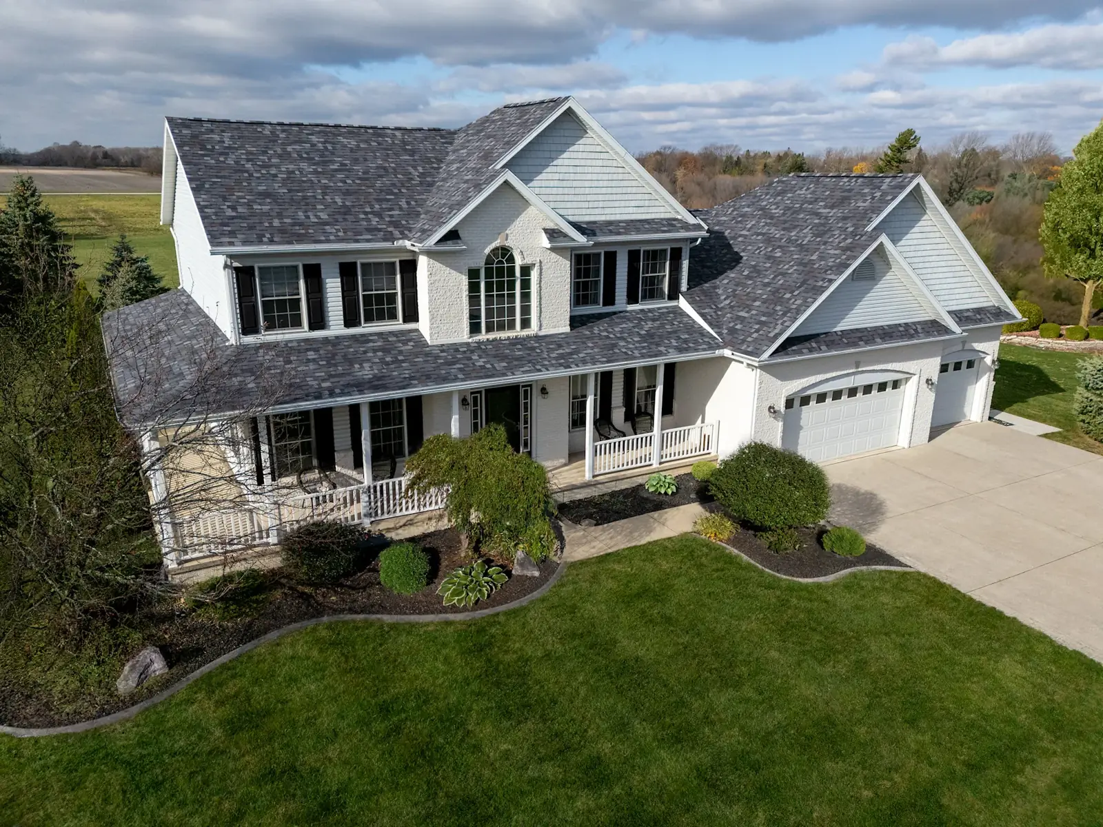 White farmhouse with a dimensional gray shingle roof and wraparound porch