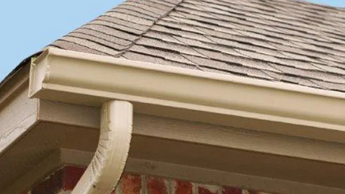Cream-colored gutter and downspout following the corner of a shingle roof