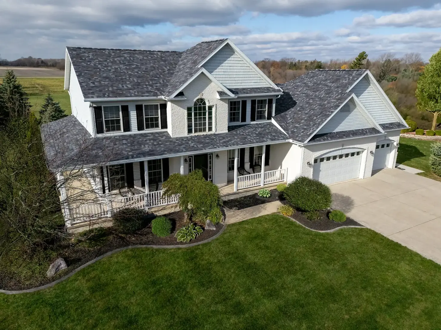 White farmhouse with a dimensional gray shingle roof and wraparound porch