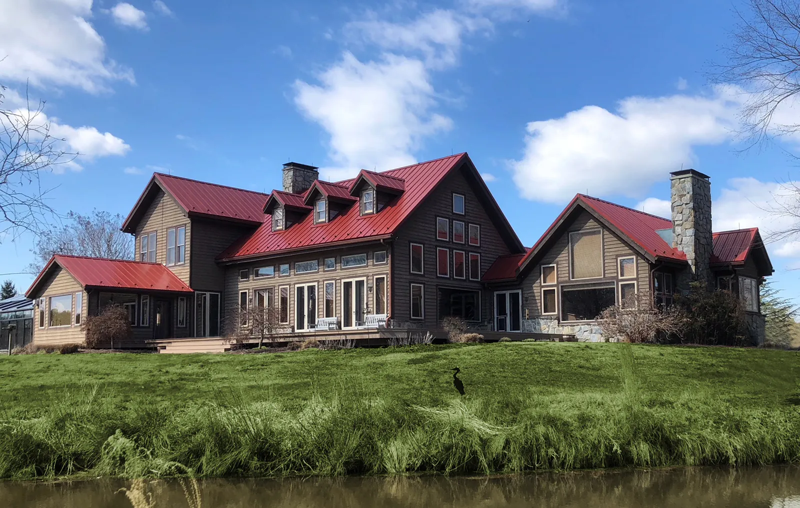 Red standing seam metal roof on a large wood-and-stone home with a green lawn